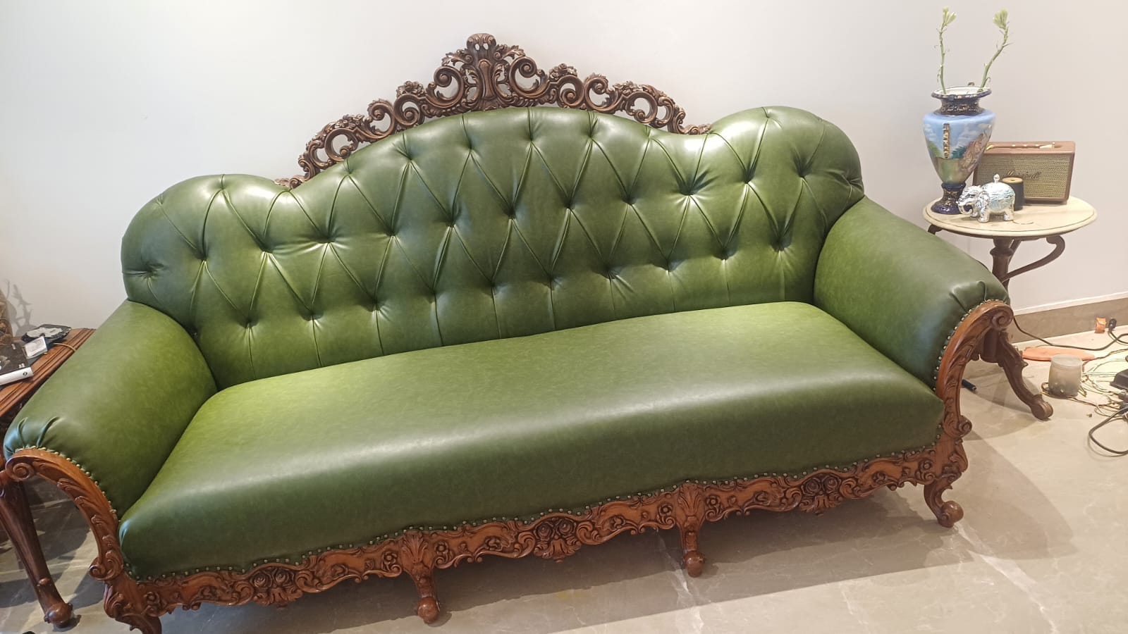A green tufted leather sofa on a hand-carved wooden frame